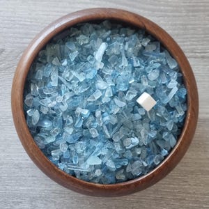 May include: A wooden bowl filled with light blue aquamarine chips. A small white cube is in the centre of the bowl.