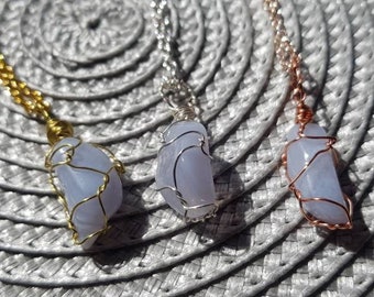 May include: Three necklaces with blue agate stones wrapped in wire. The necklaces are on a white, circular, woven surface. The wire is gold, silver, and copper.
