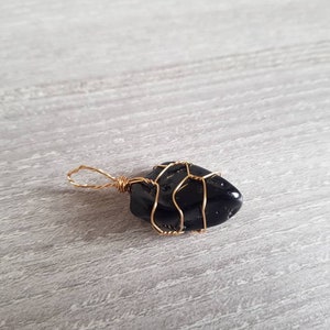 May include: A black gemstone wrapped in gold wire, creating a pendant.