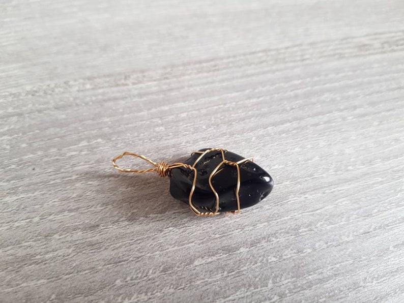 May include: A black gemstone wrapped in gold wire, creating a pendant.