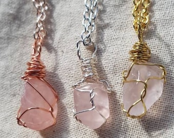 May include: Three rose quartz necklaces with different colored chains. The necklaces feature a rose quartz pendant wrapped in wire. The chains are gold, silver, and rose gold.