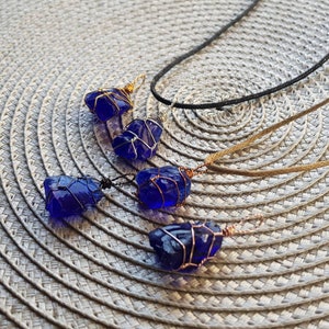 May include: Four cobalt blue sea glass pendants wrapped in copper wire, hanging from cords on a woven surface.