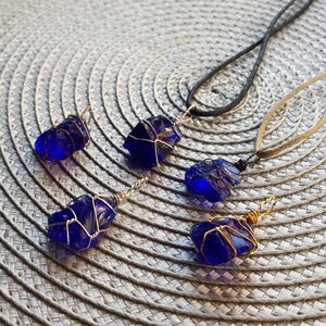 May include: Five cobalt blue glass pendants wrapped in gold wire, some on black and brown cords.