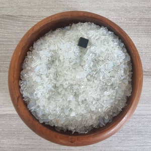 Könnte beinhalten: Eine Holzschale gefüllt mit schimmernden weißen und klaren Glassplittern. Ein kleines schwarzes Quadrat liegt auf den Glassplittern.