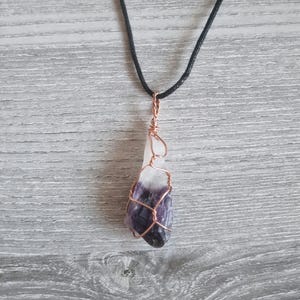 May include: A purple and white amethyst crystal wrapped in copper wire, hanging from a black cord necklace.