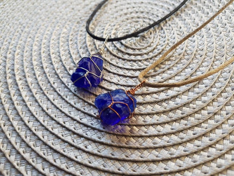 May include: Two necklaces with blue glass pendants wrapped in silver wire. One necklace has a brown cord and the other has a black cord.