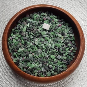 Peut inclure: Un bol en bois rempli de petits éclats de pierres précieuses vertes et noires. Les éclats sont de forme irrégulière.