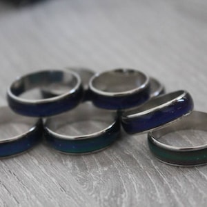 Può includere: Un gruppo di sei anelli dell'umore argentati con una pietra che cambia colore blu e verde. Gli anelli sono impilati uno sopra l'altro.