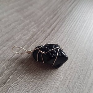 May include: A black stone pendant wrapped in silver wire. The stone is irregularly shaped and has a rough texture.