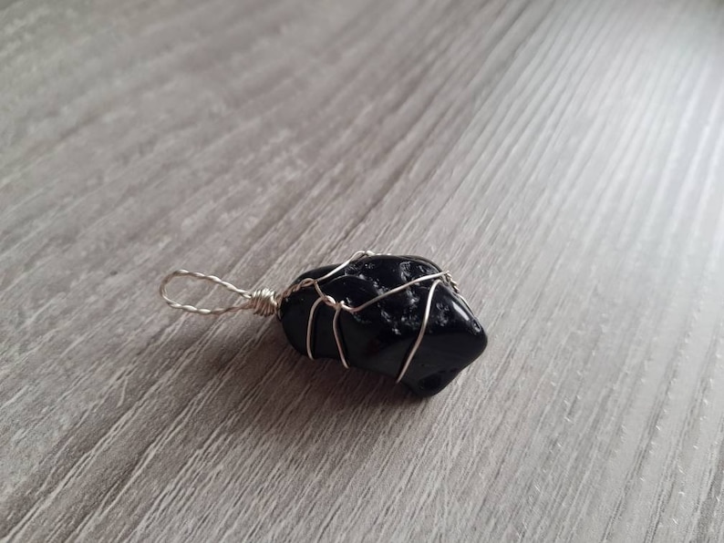 May include: A black stone pendant wrapped in silver wire. The stone is irregularly shaped and has a rough texture.