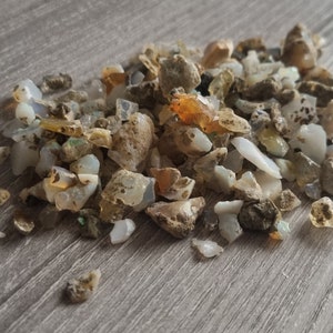 May include: A pile of small, rough, white, brown, and orange opal stones on a wooden surface.