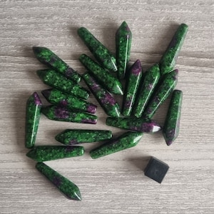 May include: A collection of green and purple gemstone points, also known as zoisite, arranged on a grey wooden surface.