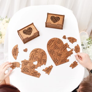 Puede incluir: Un rompecabezas de madera en forma de coraz&oacute;n con mensajes grabados para una pareja. El rompecabezas est&aacute; hecho de dos piezas que encajan para formar un coraz&oacute;n completo. Las piezas est&aacute;n esparcidas sobre una mesa blanca con dos peque&ntilde;as cajas de madera con recortes en forma de coraz&oacute;n.