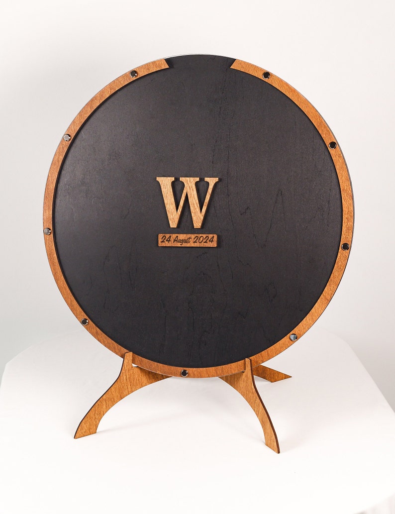 May include: A round wooden sign with a black center and a wooden stand. The sign has a large wooden letter "W" and the date "24 August 2024" written on it.