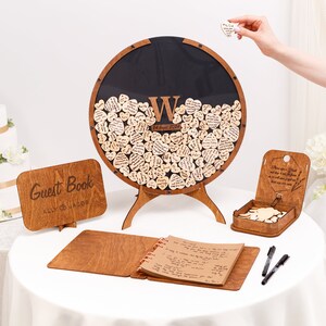 May include: A wooden guest book set with a heart-shaped wooden guest book, a wooden sign that says "Guest Book Ally & Jacob", a wooden guest book with a brown cover, and two black pens.