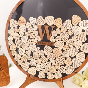 May include: A wooden heart-shaped guest book with a black chalkboard background. The hearts are filled with handwritten messages and the date "24 August 2024" is written on the chalkboard.