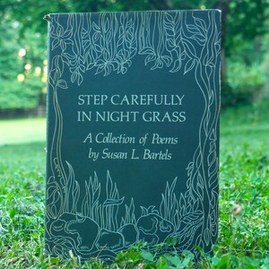 May include: A hardcover book titled "STEP CAREFULLY IN NIGHT GRASS" with white text and floral illustrations on a dark teal background. The book is a collection of poems by Susan L. Bartels. The cover art features detailed line drawings of leaves and plants.