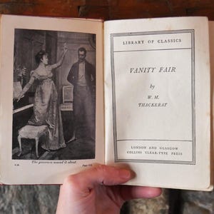 Könnte beinhalten: Offenes Buch mit einer Schwarz-Weiß-Illustration und Text. Die Illustration zeigt eine Frau und einen Mann in einem Raum. Der Text auf der rechten Seite lautet "VANITY FAIR" von W.M. Thackeray.