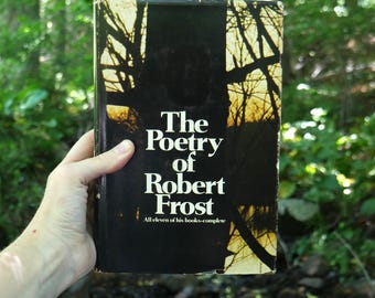 May include: A hardcover book titled The Poetry of Robert Frost, All eleven of his books-complete. The cover features a black and white graphic of tree silhouettes against a light background. The book has a rectangular shape with white text.