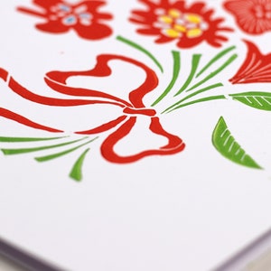 May include: A white card with a red and green floral design. The design features a large red bow with green leaves and stems.
