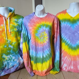 May include: Three tie-dye shirts in different styles: a long-sleeved hoodie, a long-sleeved crew neck, and a short-sleeved v-neck. The shirts feature a swirl pattern in shades of pink, yellow, green, and blue.
