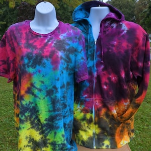 May include: A tie-dye t-shirt and a zip-up hoodie in a range of colours including pink, purple, blue, green, yellow, and black. The hoodie has a hood and pockets. Both items are displayed on mannequins, showcasing the tie-dye design.