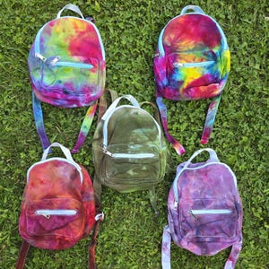May include: Five small backpacks with light blue zippers and trim. The top left bag is yellow, pink, and green tie-dye. The top right is red, yellow, and blue tie-dye. The center bag is olive green. The bottom left is red and orange, and the bottom right is purple.