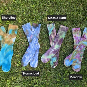 Peut inclure: Quatre paires de chaussettes montantes c&ocirc;tel&eacute;es avec des motifs tie-dye &eacute;tiquet&eacute;s Shoreline, Stormcloud, Moss & Bark et Meadow. Les chaussettes pr&eacute;sentent diverses combinaisons de couleurs dont bleu, marron, violet, vert et rose.