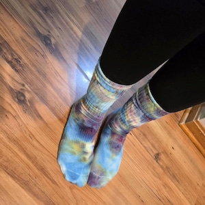 Peut inclure: Une paire de chaussettes mi-mollet avec un motif tie-dye aux nuances m&eacute;lang&eacute;es de bleu clair, de violet profond et de jaune doux. Les chaussettes pr&eacute;sentent une texture c&ocirc;tel&eacute;e au niveau de la cheville et du pied, avec un design tourbillonnant.