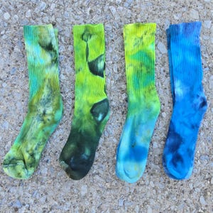 Peut inclure: Quatre chaussettes mi-mollet avec des motifs tie-dye dans des tons de vert, jaune et bleu. La premi&egrave;re est vert citron et sarcelle, la deuxi&egrave;me est jaune vif et vert for&ecirc;t fonc&eacute;, la troisi&egrave;me est jaune et bleu, et la quatri&egrave;me est bleue.