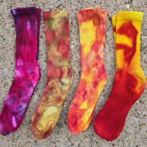 Peut inclure: Quatre chaussettes mi-mollet avec des motifs tie-dye. La premi&egrave;re est magenta fonc&eacute; et violette, la deuxi&egrave;me est un m&eacute;lange de jaune et d'orange, la troisi&egrave;me est jaune vif et orange, et la quatri&egrave;me est une combinaison vibrante de jaune et rouge.