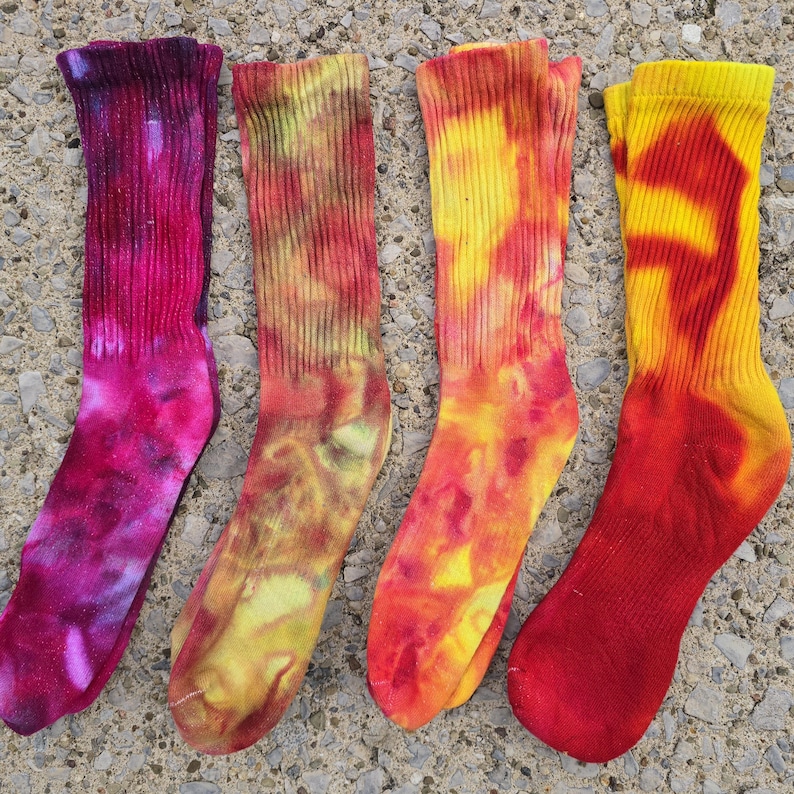 Peut inclure: Quatre chaussettes mi-mollet avec des motifs tie-dye. La premi&egrave;re est magenta fonc&eacute; et violette, la deuxi&egrave;me est un m&eacute;lange de jaune et d'orange, la troisi&egrave;me est jaune vif et orange, et la quatri&egrave;me est une combinaison vibrante de jaune et rouge.