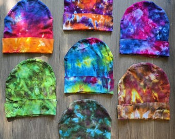 Peut inclure: Sept bonnets présentant des motifs tie-dye vibrants dans diverses combinaisons de couleurs, notamment violet, orange, bleu, vert et marron. Chaque bonnet possède un revers plié à la base et une calotte arrondie, avec des motifs teintés.
