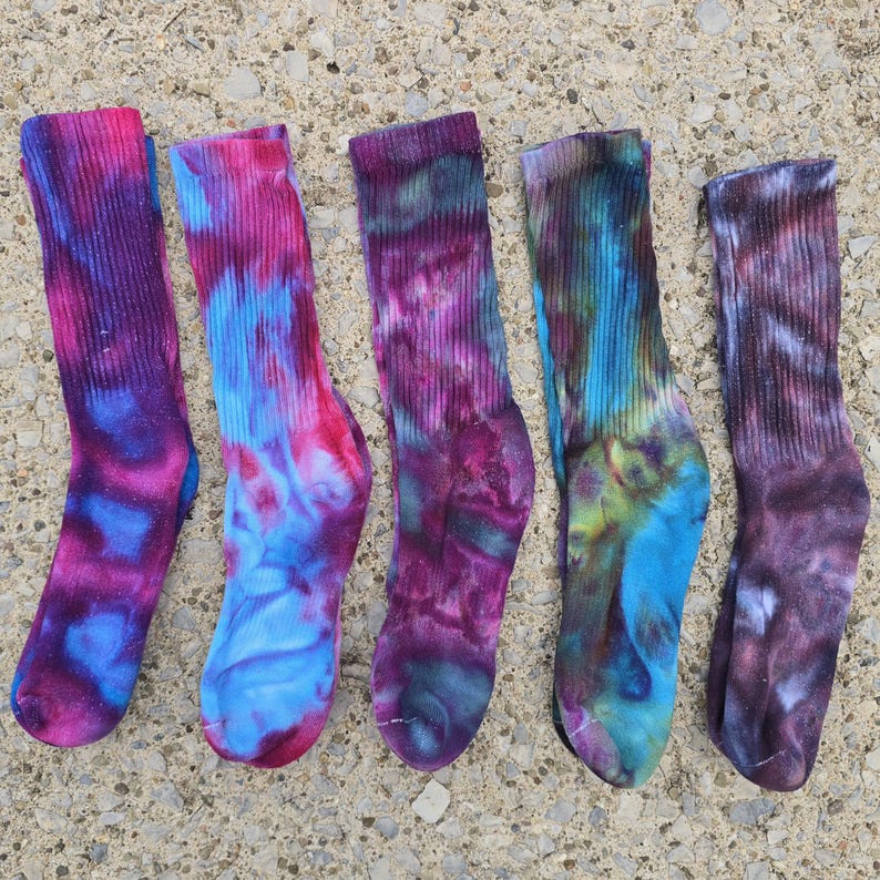 Peut inclure: Cinq chaussettes mi-mollet avec des motifs tie-dye dans diverses combinaisons de couleurs. Les chaussettes pr&eacute;sentent des teintes m&eacute;lang&eacute;es de magenta, bleu vif, violet profond, sarcelle et gris anthracite, avec une texture c&ocirc;tel&eacute;e sur la tige.