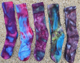 Peut inclure: Cinq chaussettes mi-mollet avec des motifs tie-dye dans diverses combinaisons de couleurs. Les chaussettes présentent des teintes mélangées de magenta, bleu vif, violet profond, vert forêt et gris anthracite, avec des bords côtelés et un tissu texturé.