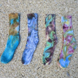 Peut inclure: Quatre chaussettes montantes avec des motifs tie-dye. La premi&egrave;re chaussette pr&eacute;sente des tons marron et bleu. La deuxi&egrave;me affiche des nuances de bleu et de gris. La troisi&egrave;me montre des teintes vertes, violettes et bleues. La quatri&egrave;me est rose, jaune et bleue.