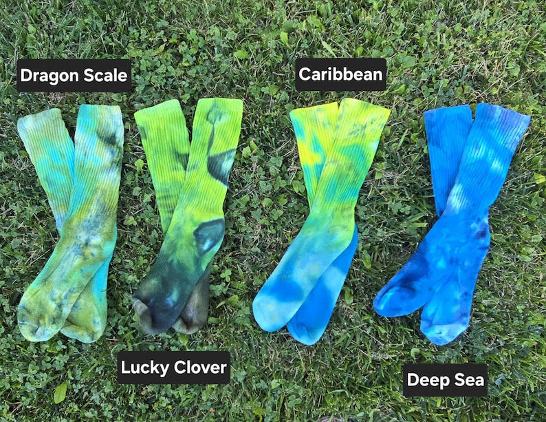 Peut inclure: Quatre paires de chaussettes montantes tie-dye dispos&eacute;es en rang&eacute;e. La premi&egrave;re paire est &eacute;tiquet&eacute;e Dragon Scale avec des tons verts et jaunes. La deuxi&egrave;me, Lucky Clover, pr&eacute;sente des motifs vert fonc&eacute;. La troisi&egrave;me, Caribbean, montre du jaune et du bleu, et la quatri&egrave;me, Deep Sea, affiche des nuances de bleu.