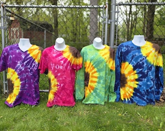 Peut inclure: Quatre t-shirts tie-dye présentés sur des mannequins. Le premier est violet avec un motif de tournesol jaune et marron. Le deuxième est rose avec un motif de tournesol jaune et marron. Les troisième et quatrième sont verts et bleus.