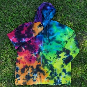 May include: A colourful tie-dye zip-up hoodie. The hoodie displays a mix of colours, including purple, blue, green, yellow, orange, and red. It has a full zip, a hood, and pockets. The garment is made of a soft material.