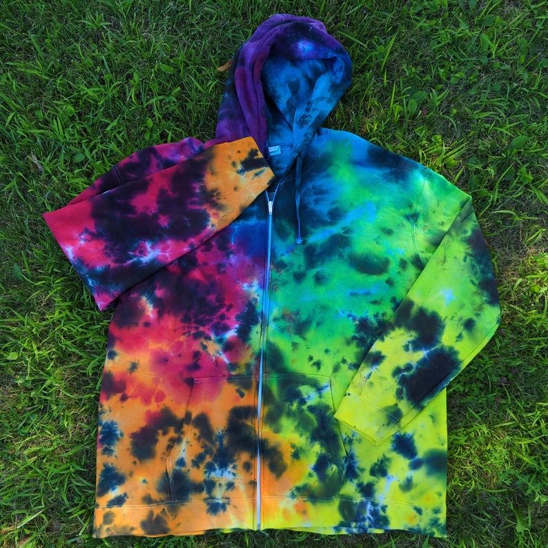 May include: A colourful tie-dye zip-up hoodie. The hoodie displays a mix of colours, including purple, blue, green, yellow, orange, and red. It has a full zip, a hood, and pockets. The garment is made of a soft material.