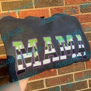 May include: A dark gray sweatshirt with the word "MAMA" in green, black, and white stripes with dripping green accents.