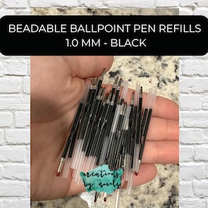 May include: A collection of black ballpoint pen refills with clear plastic tubes, held in a hand. The text on the black banner reads: BEADABLE BALLPOINT PEN REFILLS 1.0 MM - BLACK.