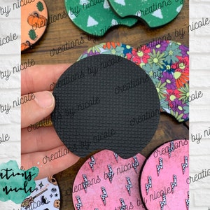 May include: A set of six round coasters with various designs. The coasters are made of a cork-like material with a black rubber backing. The designs include a floral pattern, a lightning bolt pattern, a pumpkin pattern, a witch pattern, and a Christmas tree pattern.