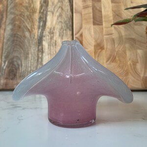 May include: A small, clear glass vase with a pink and white ombre effect. The vase has a unique, flower-like shape with four petals.