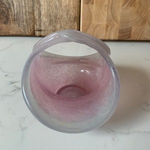 May include: A pink glass bowl with a white handle. The bowl has a speckled, marbled effect.