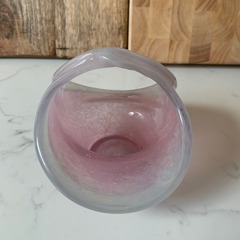 May include: A pink glass bowl with a white handle. The bowl has a speckled, marbled effect.