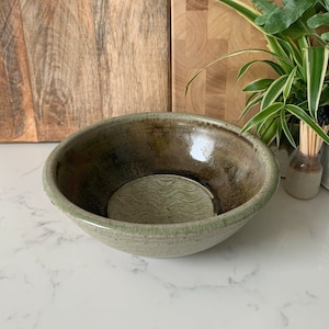 May include: A large, green ceramic bowl with a wavy pattern on the inside. The bowl has a dark brown glaze on the rim and a light brown glaze on the outside.