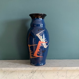 May include: A blue ceramic vase with abstract designs in white, black, and orange. The vase has a rounded body and a narrow neck.