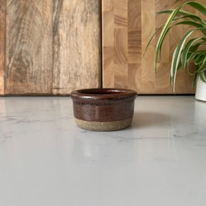May include: A small, brown ceramic bowl with a light brown rim. The bowl is sitting on a white countertop.