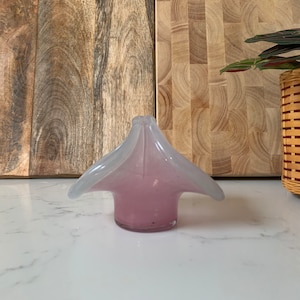 May include: A light pink and white glass flower vase with a unique, organic shape. The vase has a wide, open top and a narrow base.